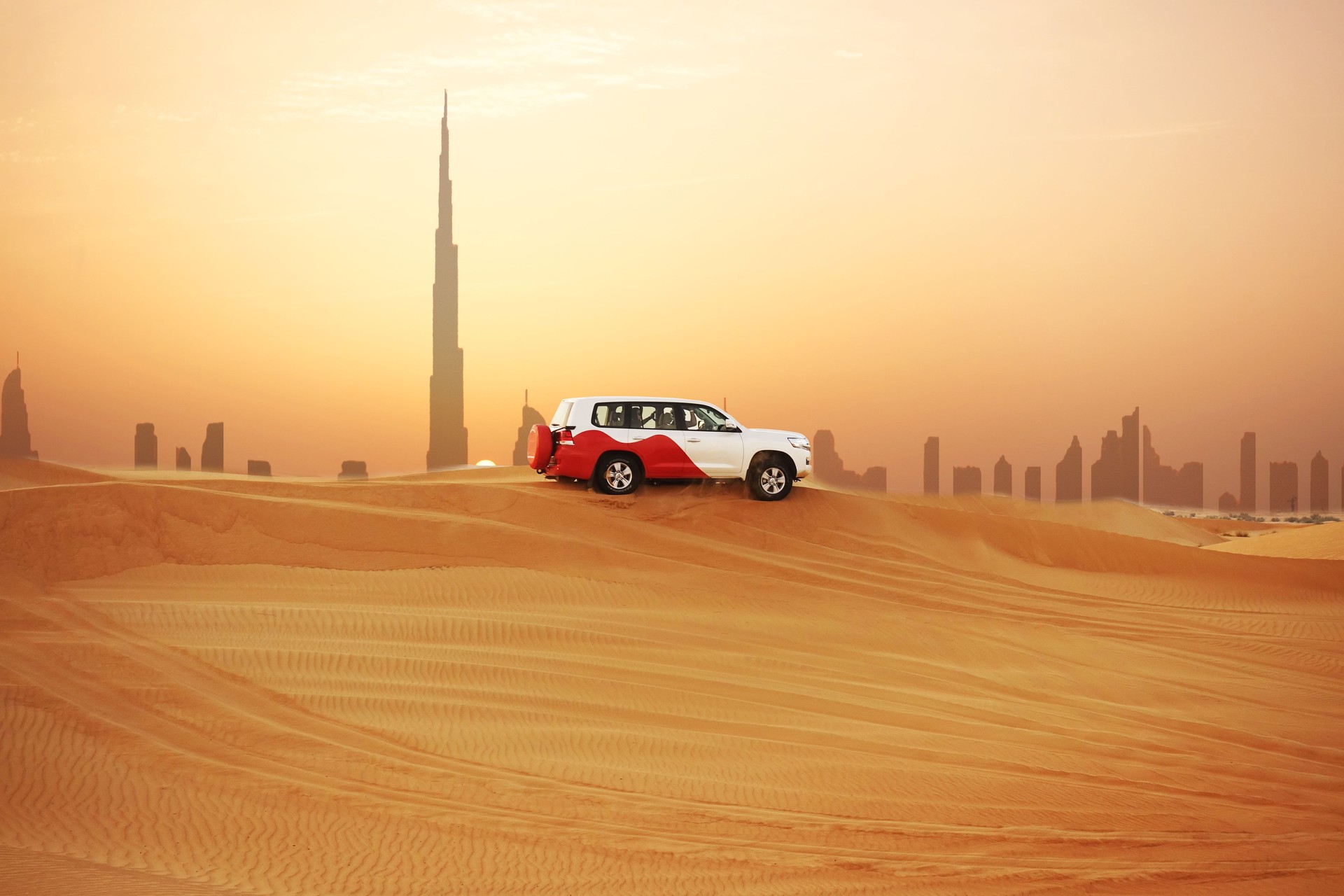 Off-road adventure with SUV in Arabian Desert at sunset with Dubai skyline or cityscape